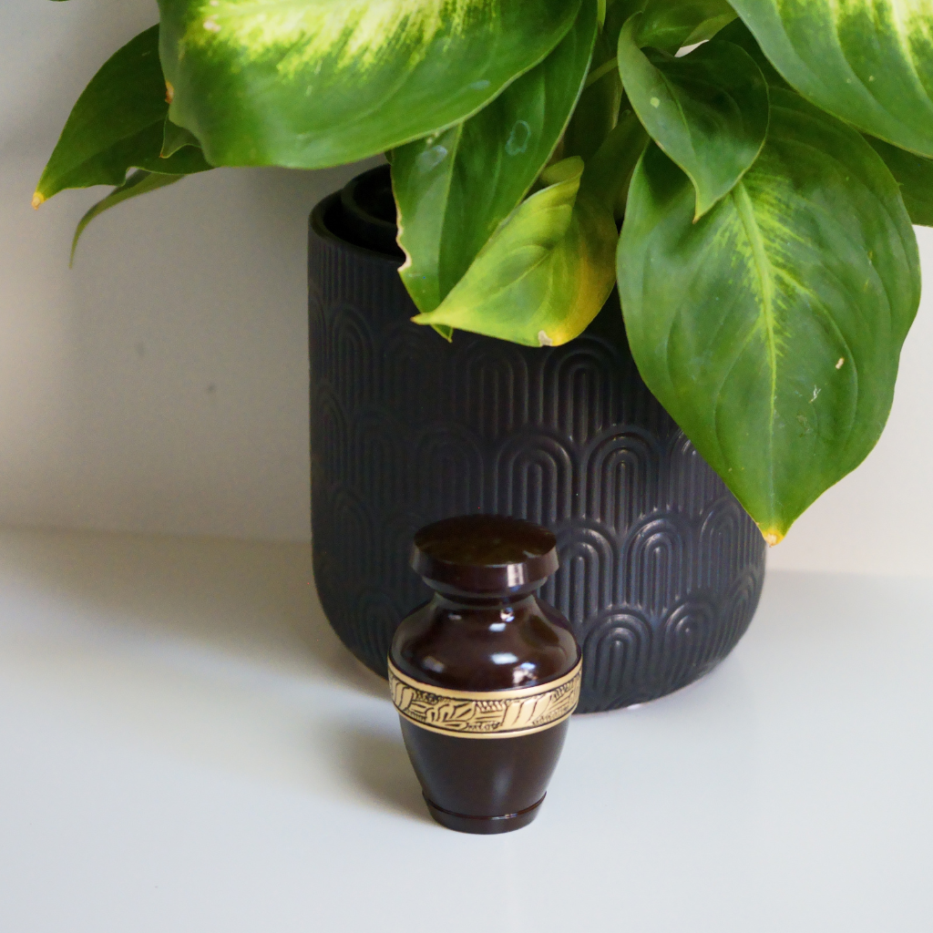 Brown keepsake urn with gold leaf detailed band in natural setting