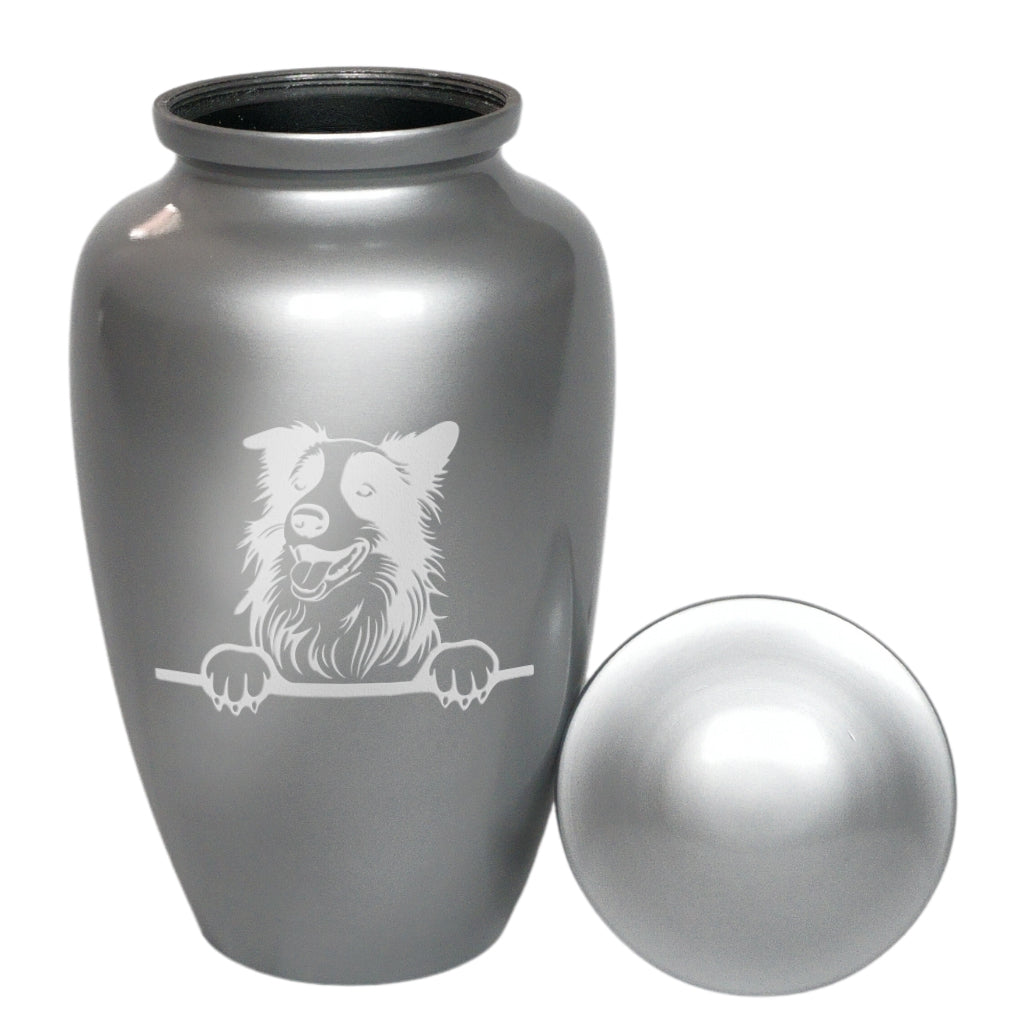A metallic silver pet memorial urn with a matching lid, featuring a white engraved illustration of a dog peeking over a bar. The urn is shown next to its lid on a plain white background.
